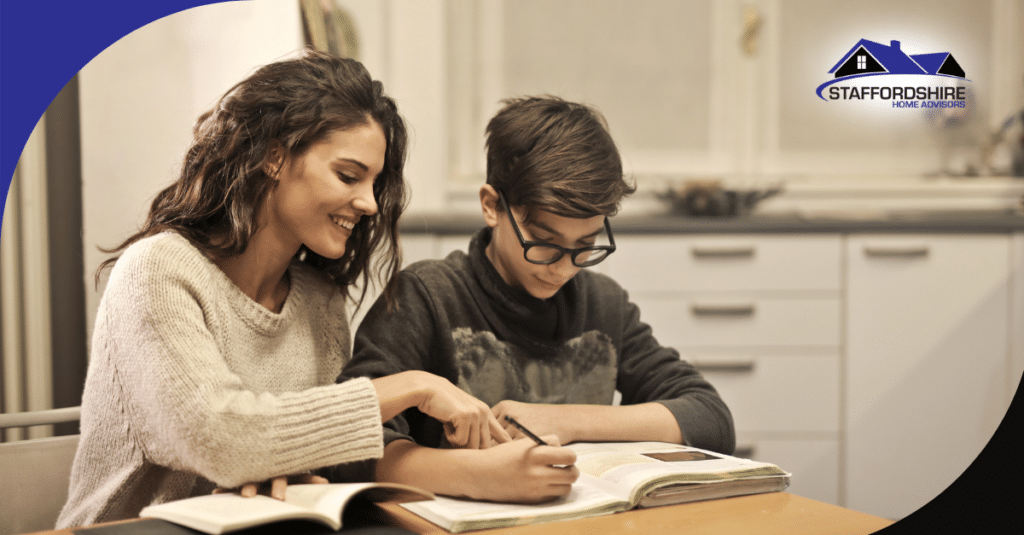 Smiling woman helping a boy with his homework at the kitchen table.