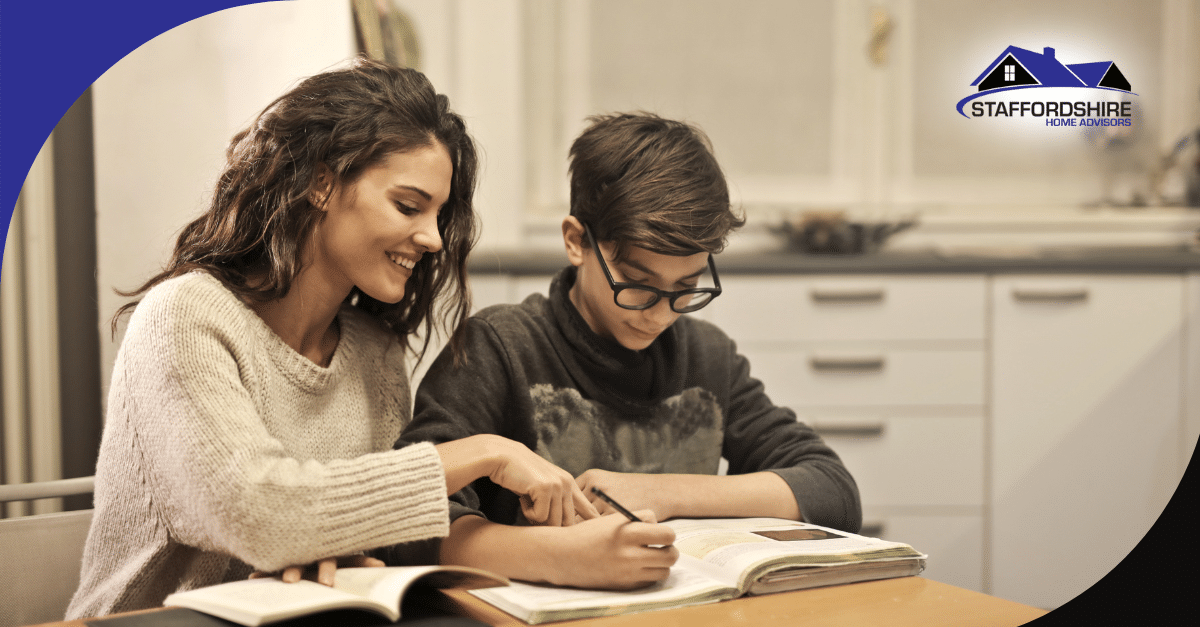Smiling woman helping a boy with his homework at the kitchen table.