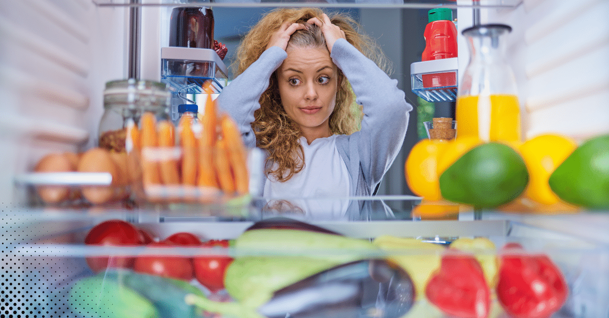 Woman looking stressed while staring into a fridge full of food.