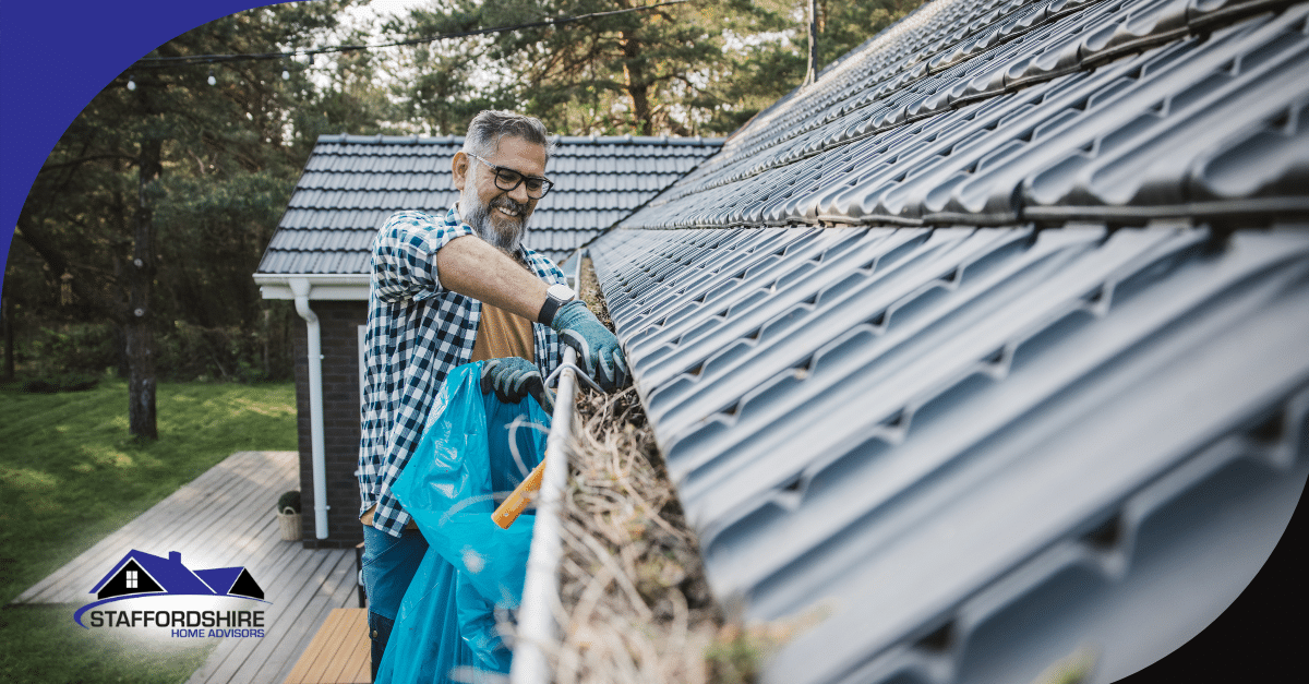 Man cleaning leaves from a roof gutter with a blue bag.