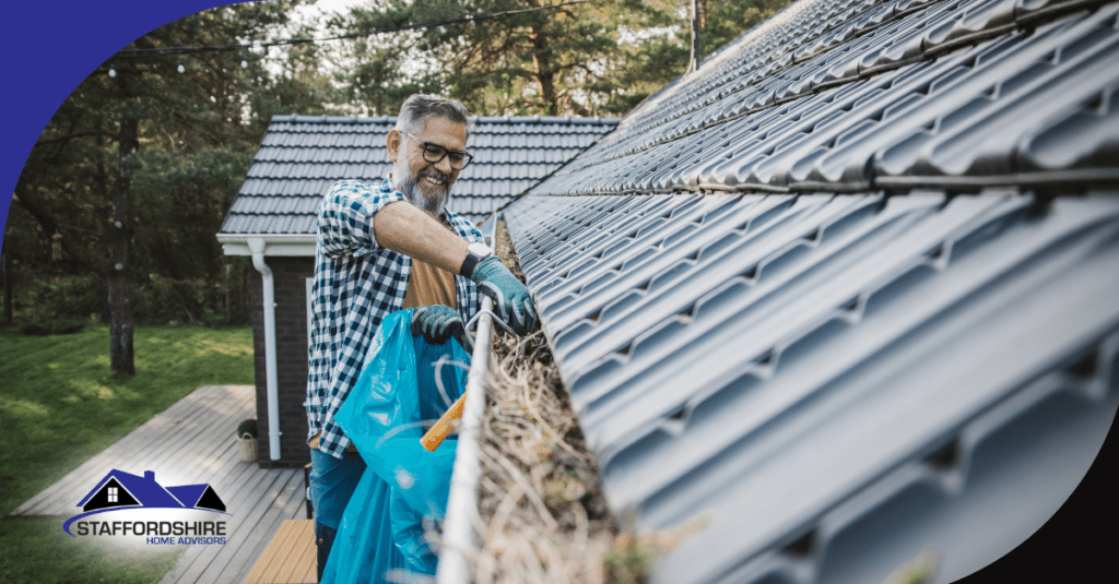 Man cleaning leaves from a roof gutter with a blue bag.