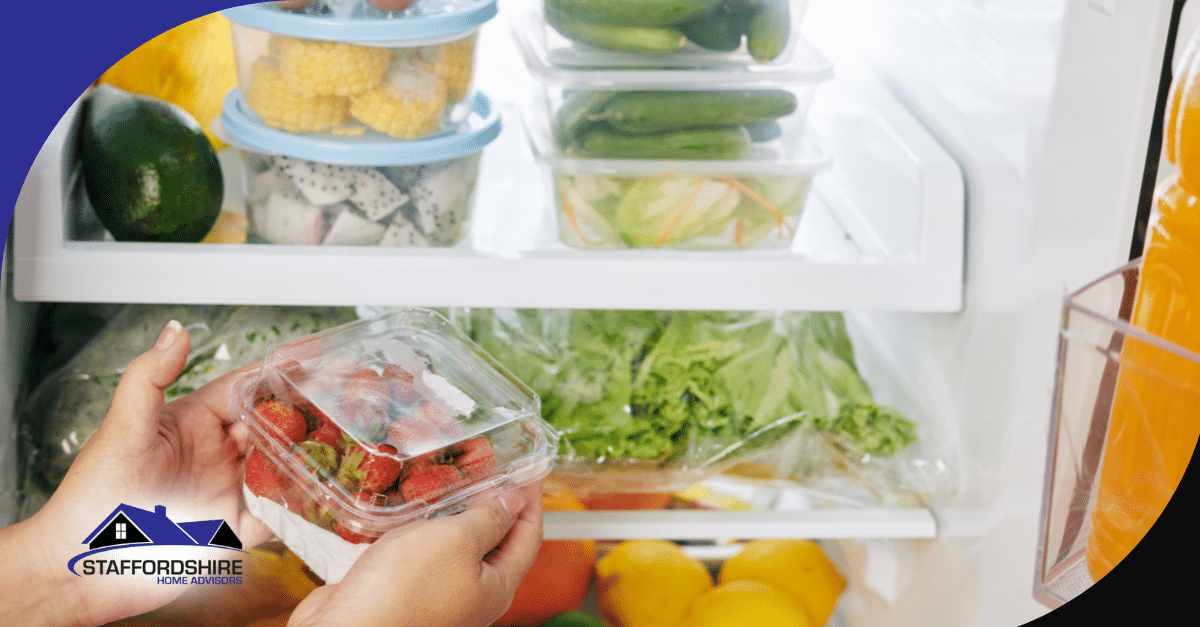 Hands placing a container of strawberries inside a refrigerator with fresh produce.