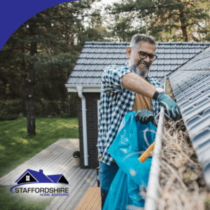 Man cleaning leaves from a roof gutter with a blue bag.