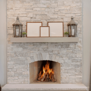 Modern stone fireplace with a burning fire, decorated mantel, and tall windows.